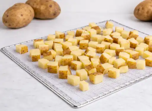 Showing a dehydrator rack with diced potatoes spread out on it
