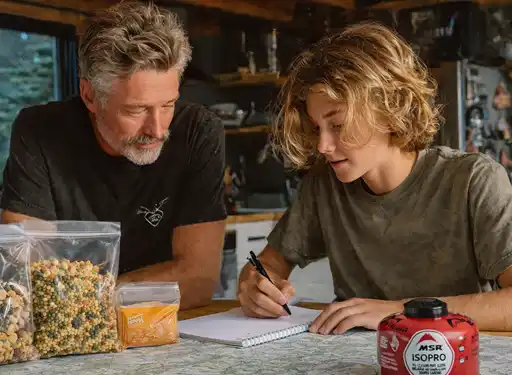 A father teaching his son at a kitchen table how to plan meals and avoid mistakes