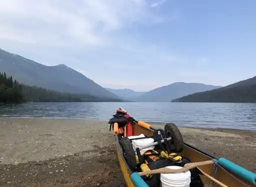 A landscape scene of one of the Bowron Lakes, surrounded by mountains and a canoe on the beach