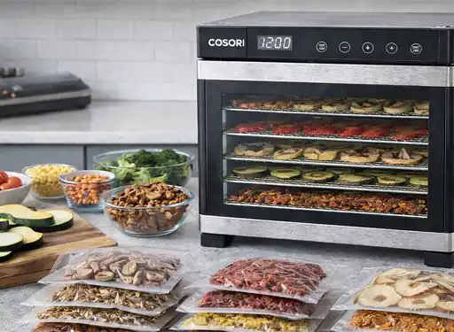 A kitchen counter showing a food dehydrator and fresh food next to vacuum-sealed food that is dehydrated