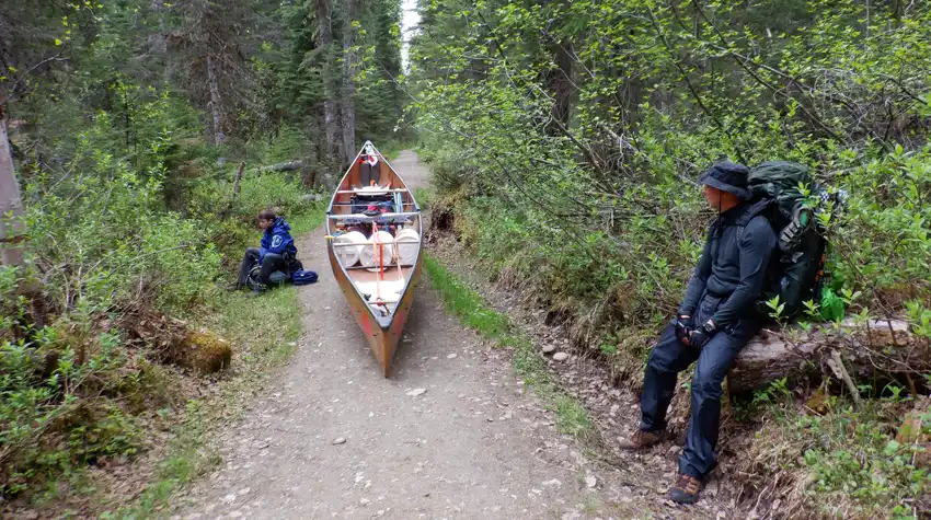 A photo showing a canoe with 3 large food pails and gear on a portage as we rested