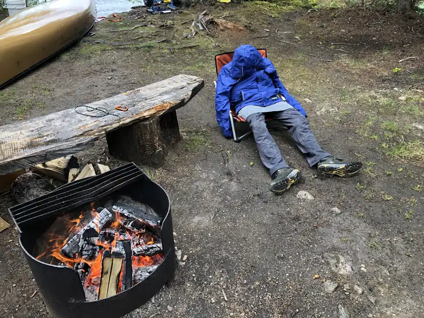 A photo of Nick passed out after a long day of paddling as he sits in a chair next to a warm fire after a rain storm hit