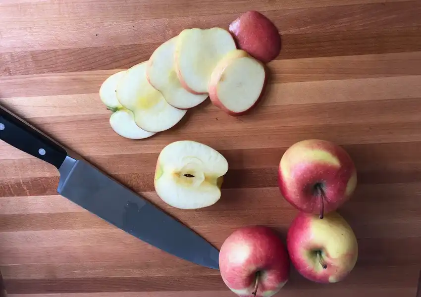 Showing apples on a cutting board with a french knife next to sliced apples