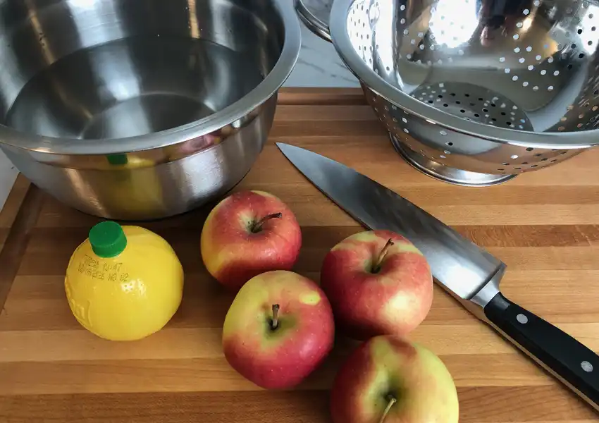 Showing Ambrosia apples next to a colander, bowl of water and lemon for preparation
