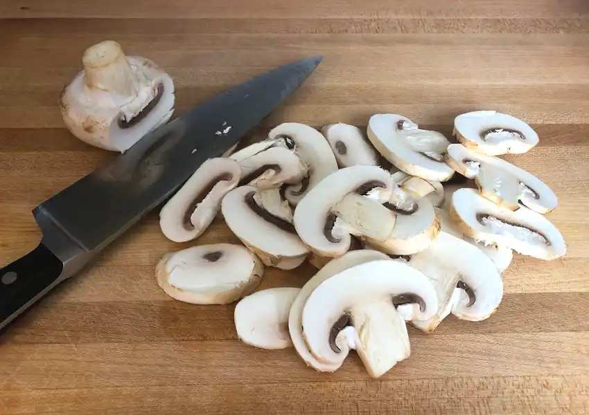 Sliced mushrooms on a cuttingboard with a french knife