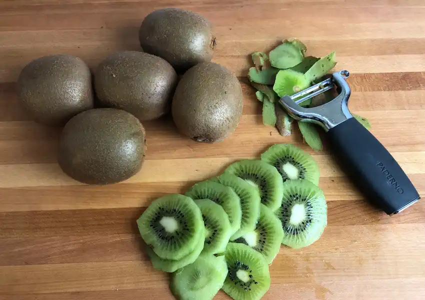 Several kiwis on a cutting board being prepped for dehydration
