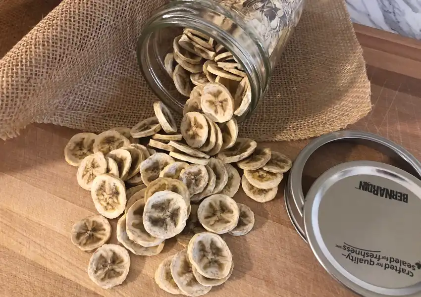 Showing dehydrated bananas in a canning mason jar on a cutting board