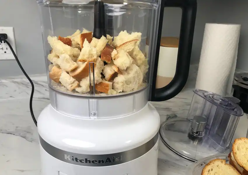 A food processor showing pieces of broken up dried bread slices