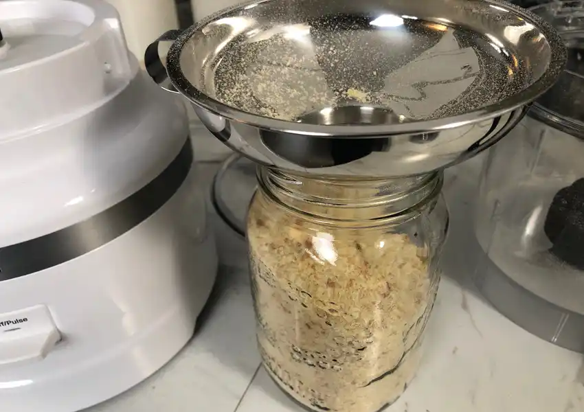 Close up of a food processor and a mason jar with a canning funnel and filled with breadcrumbs