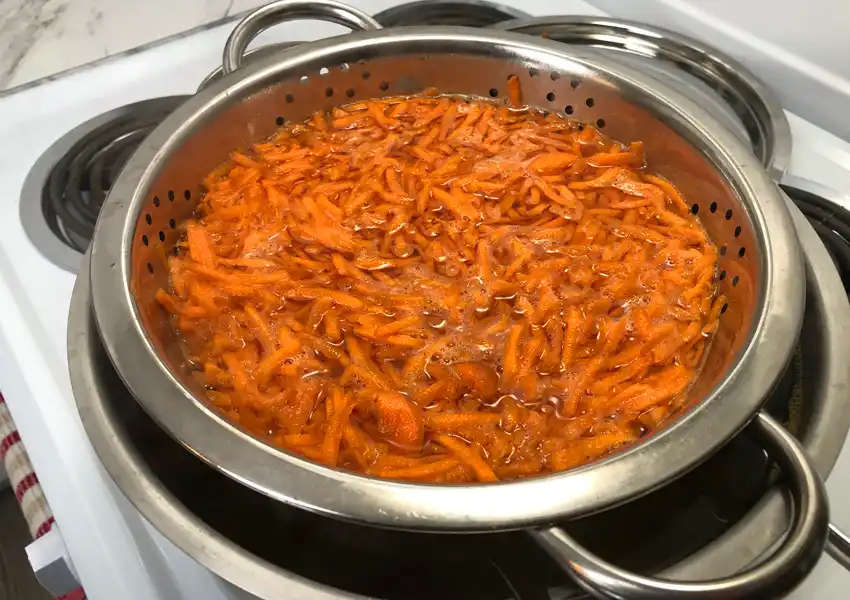 Showing a pot on the stove with shredded carrots being blanched
