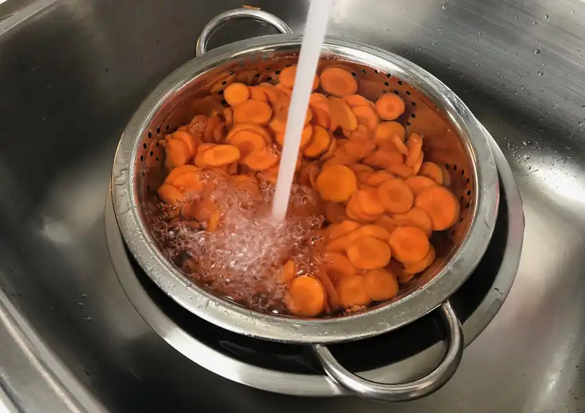A photo showing carrot coins being run under cold water to stop the cooking process