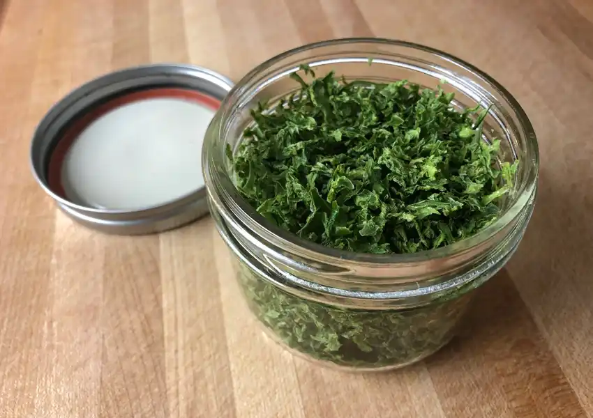 A mason jar filled with the dried jalapenos, sitting on a wooden cutting board