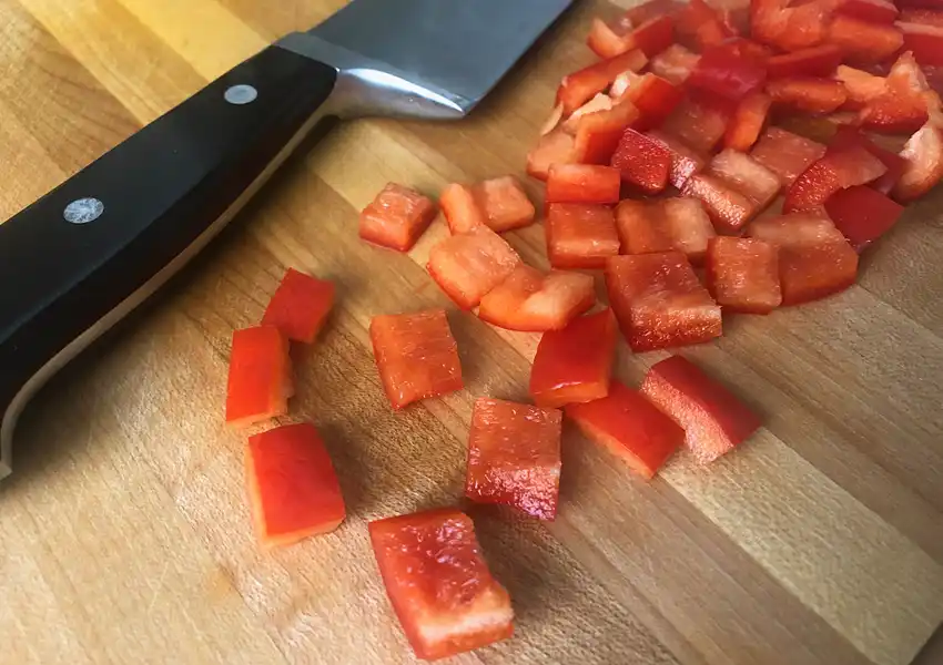 Showing peppers diced on a cutting board with a french knife
