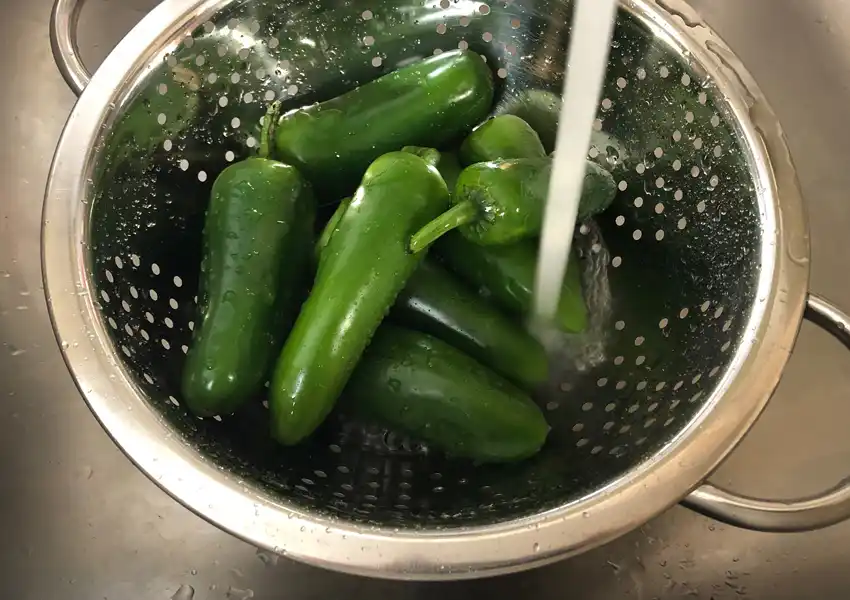 Jalapenos in a colander getting washed under cold water