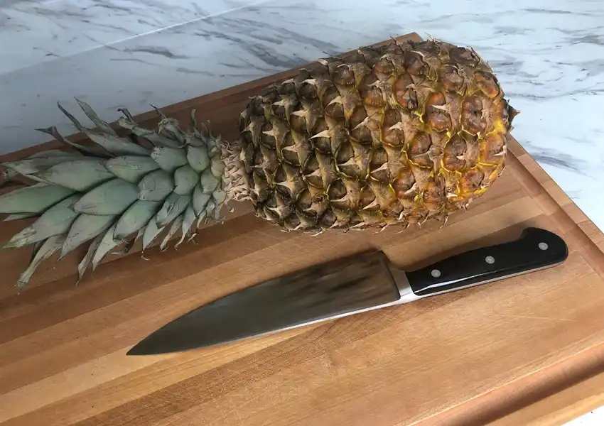 A fresh pineapple on a cuttingboard with a knife ready to be prepped