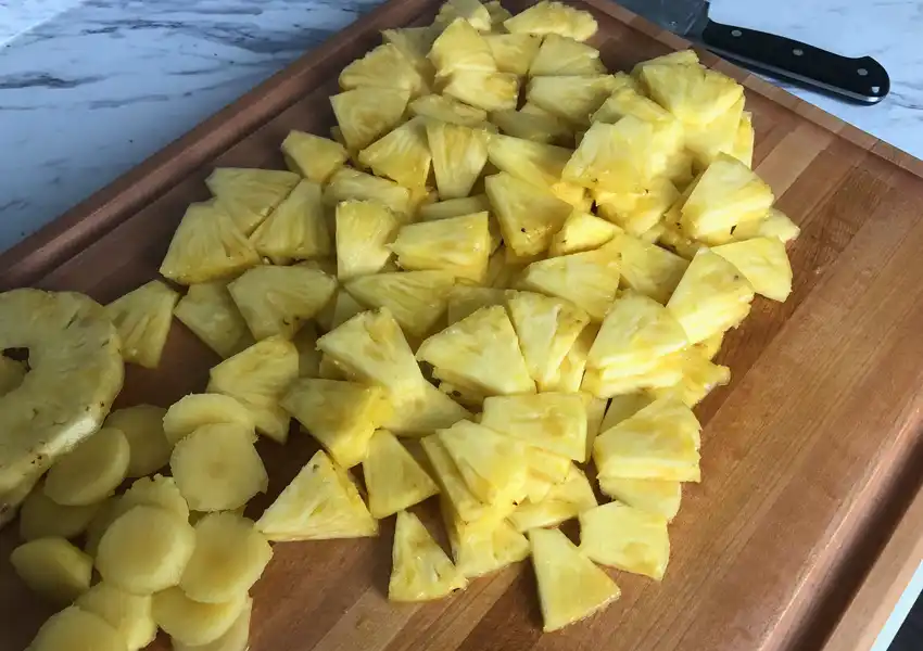 Showing fresh pineapple cut up into tidbits on a cutting board
