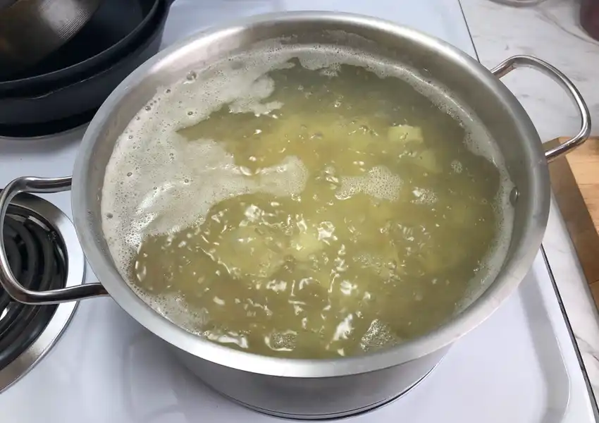 Showing diced yellow potatoes being blanched in simmering water in a pot