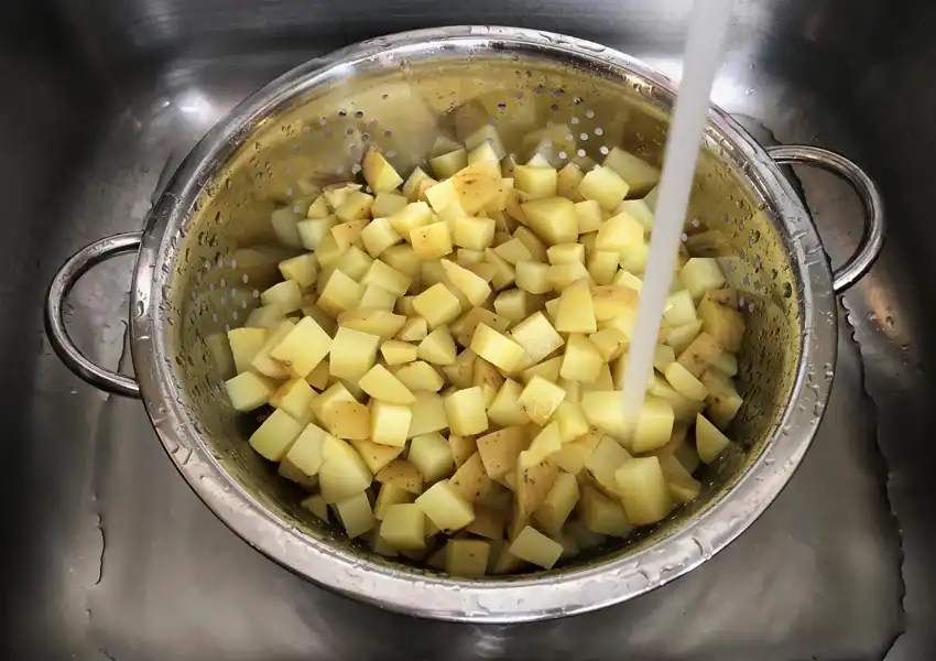 Showing the diced potatoes cooling under running cold water to stop cooking