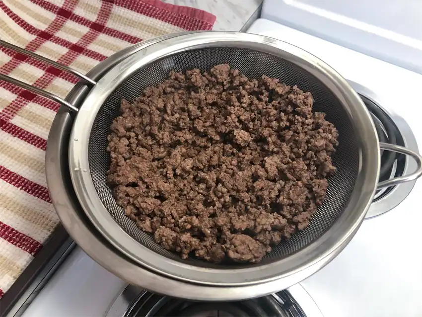 Straining cooked ground beef in a sieve to drain grease