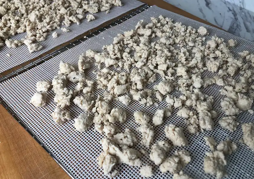 Spreading out cooked ground chicken on perforated silicon sheets for dehydrating